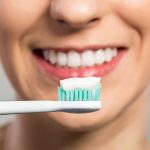 A woman cleaning her teeth with a toothbrush and toothpaste