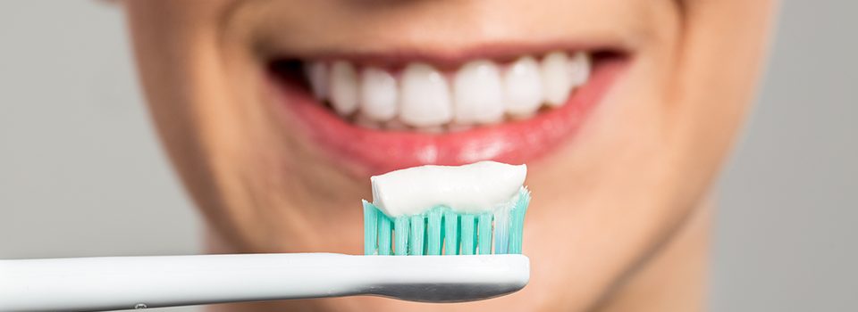 A woman cleaning her teeth with a toothbrush and toothpaste