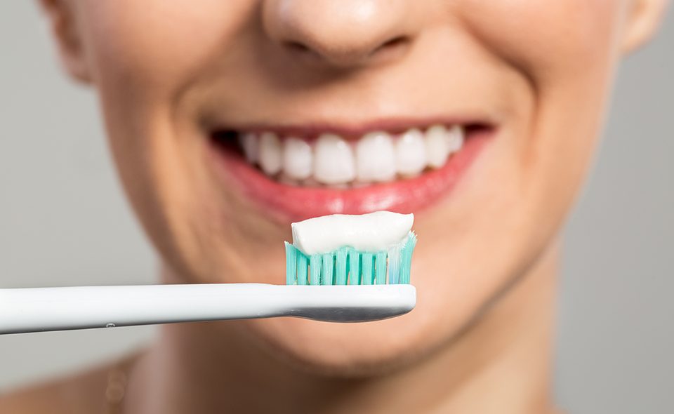 A woman cleaning her teeth with a toothbrush and toothpaste