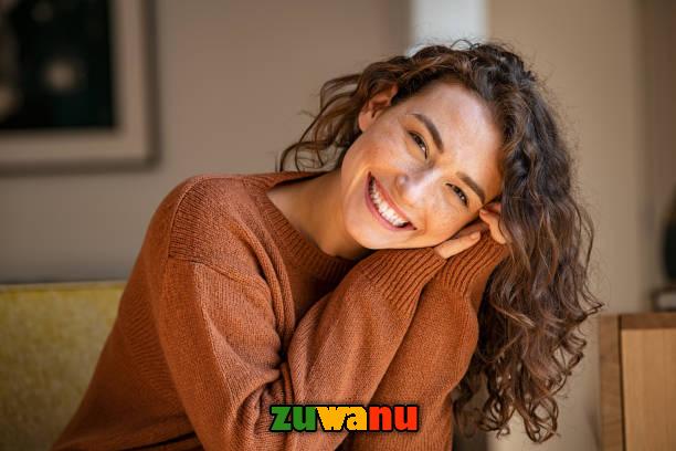 Happy young woman sitting on sofa at home and looking at camera. Portrait of comfortable woman in winter clothes relaxing on armchair. Portrait of beautiful girl smiling and relaxing during autumn. Young Without Aging